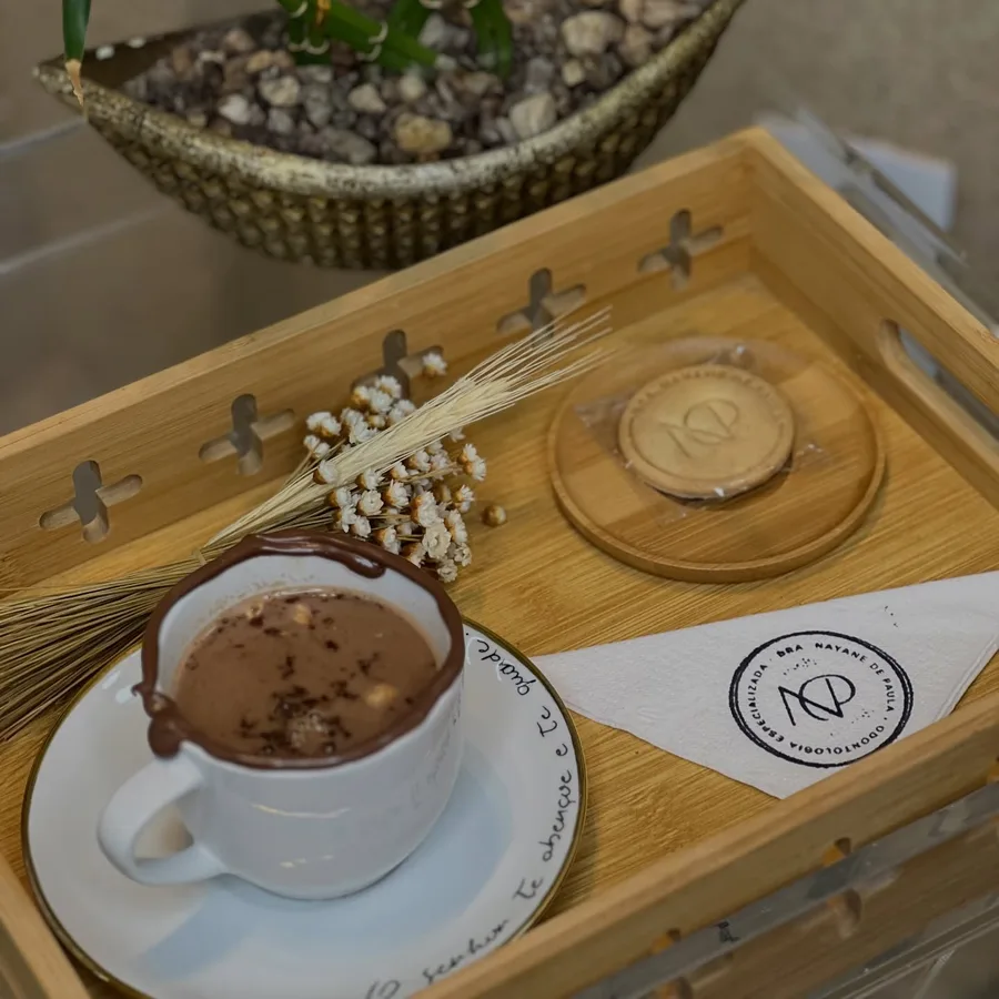 Chocolate quente e biscoito com a marca da Dra. Nayane servidos em bandeja de madeira