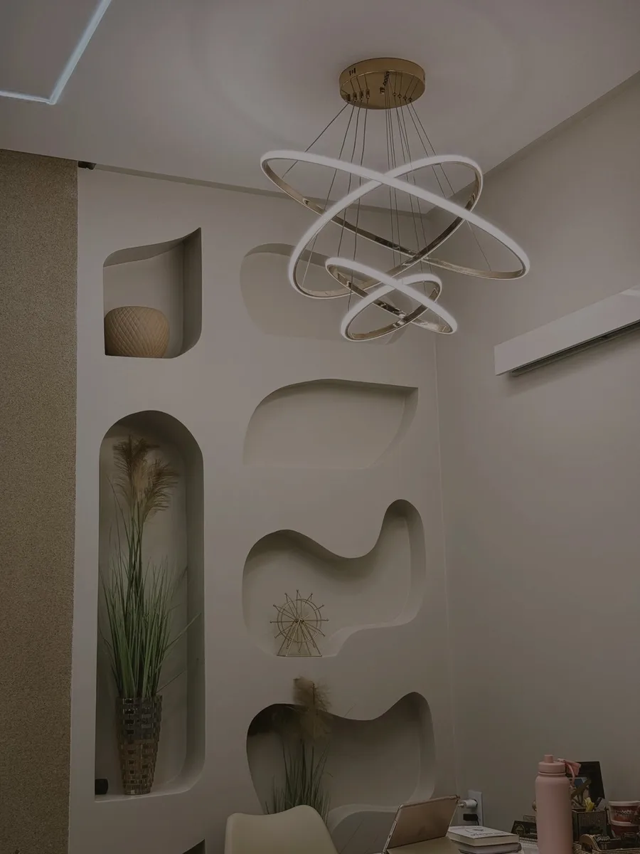 Parede com nichos orgânicos iluminados e lustre de anéis dourados