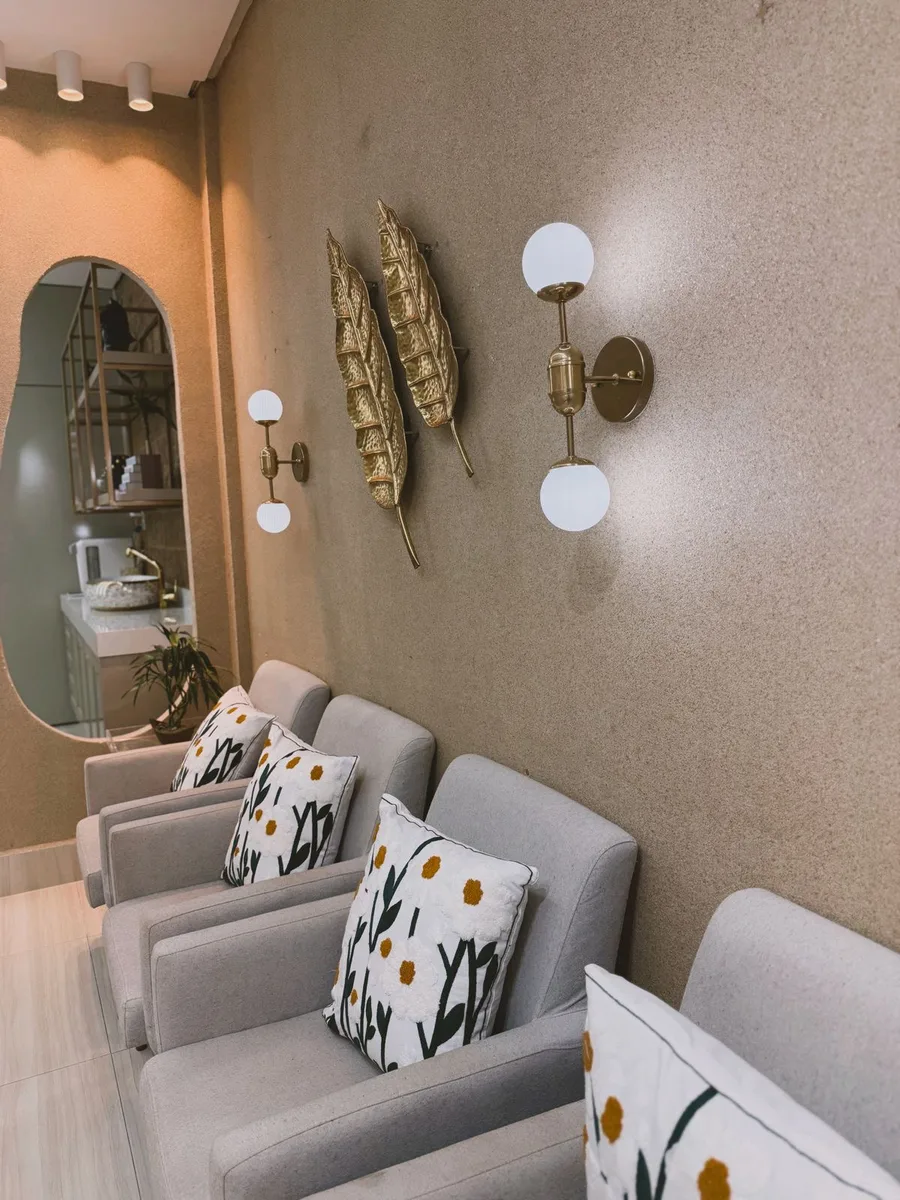Sala de espera com poltronas cinza, almofadas florais e arandelas douradas
